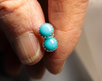 May include: A pair of silver earrings with turquoise stones. The stones are round and have a smooth, polished finish.
