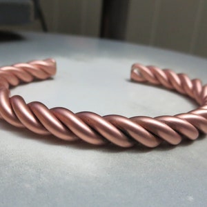 May include: A copper bracelet with a braided design. The bracelet is a simple, solid piece of jewelry.