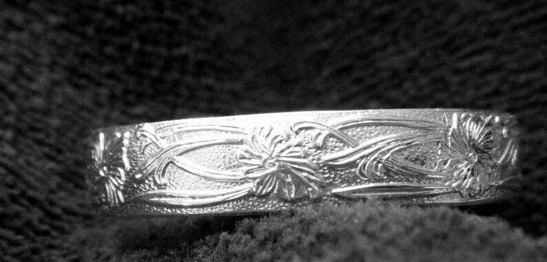 May include: A silver bangle bracelet with an intricate floral design. The bracelet is smooth and polished, with a delicate floral pattern.