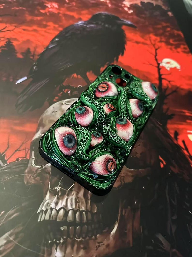 Op de afbeelding: Groene telefoonhoes met meerdere realistische oogballen met rode, blauwe en witte details. De hoes heeft een textuur, tentakelachtig ontwerp. De achtergrond bevat een raaf en een schedel, wat een griezelig thema cre&euml;ert.