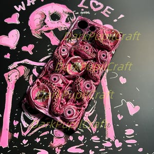 May include: A pink and black phone case with a skull and the words "What is Love!" on the back. The front of the case features a design of pink eyes and tentacles.