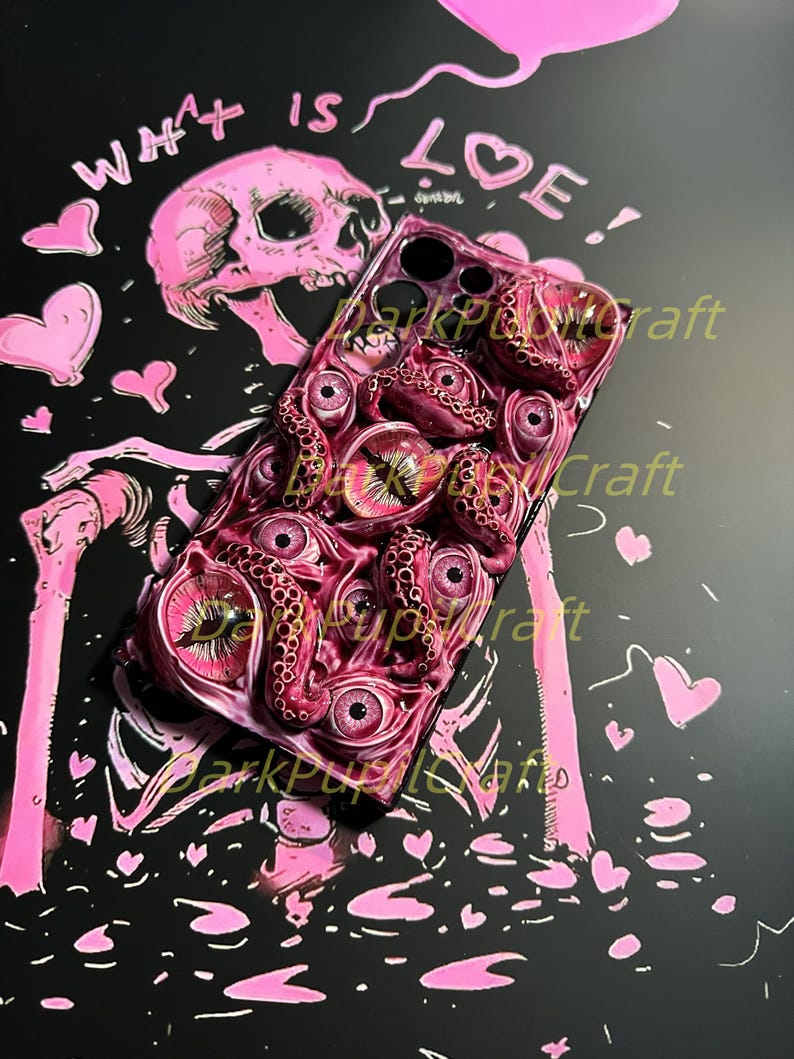 May include: A pink and black phone case with a skull and the words "What is Love!" on the back. The front of the case features a design of pink eyes and tentacles.