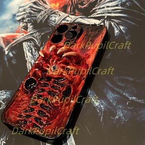 May include: A red and black iPhone case with a 3D sculpted design of a monstrous eye and tentacles. The case has the text "DarkPupilCraft" printed on it.