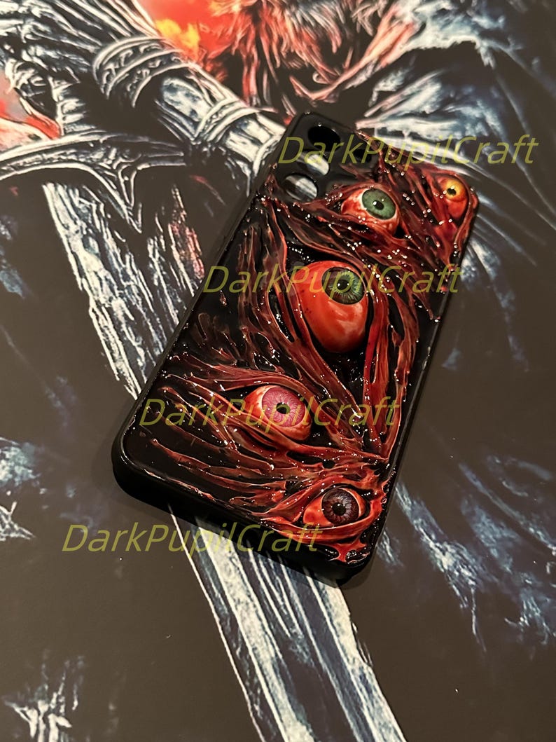 Puede incluir: Una funda de tel&eacute;fono negra con un dise&ntilde;o rojo y negro que presenta varios ojos. La funda tiene un aspecto texturizado, carnoso, con un fondo rojo oscuro y varios ojos rojos con pupilas negras.