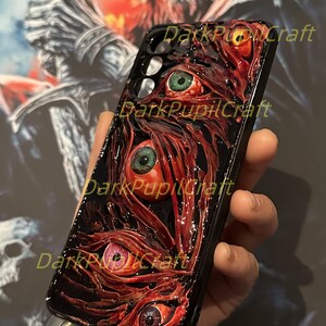Puede incluir: Carcasa de tel&eacute;fono negra con un dise&ntilde;o 3D de ojos rojos, verdes y amarillos con pupilas negras. Los ojos est&aacute;n rodeados por un dise&ntilde;o carnoso, rojo y negro.