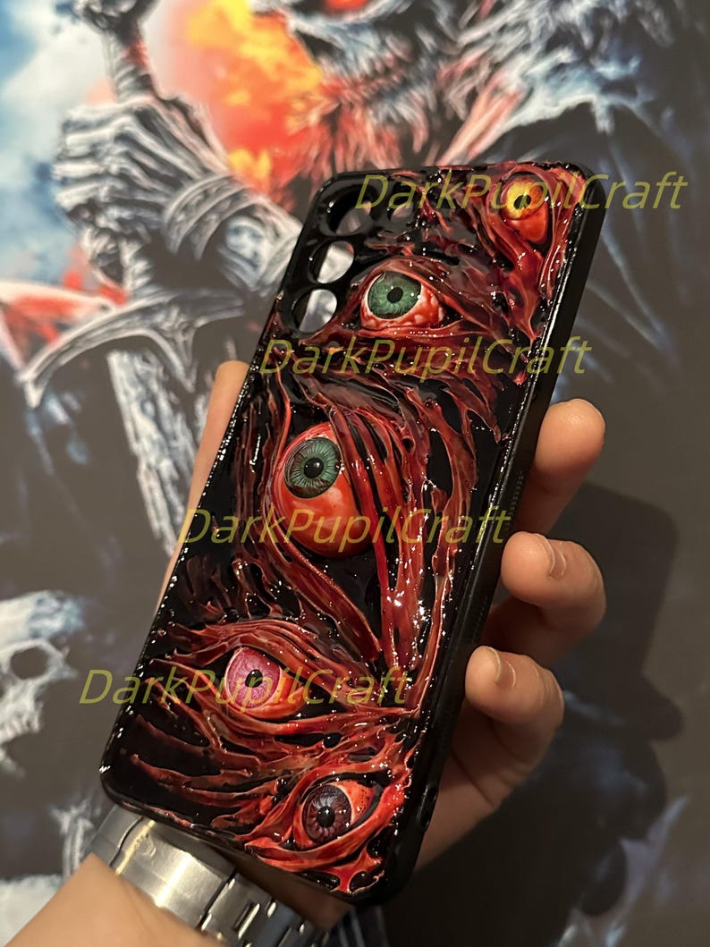 Puede incluir: Carcasa de tel&eacute;fono negra con un dise&ntilde;o 3D de ojos rojos, verdes y amarillos con pupilas negras. Los ojos est&aacute;n rodeados por un dise&ntilde;o carnoso, rojo y negro.