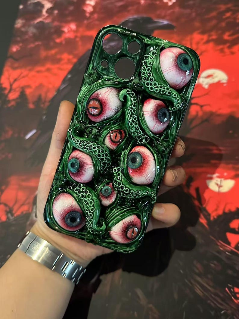 Op de afbeelding: Groene telefoonhoes met een gedetailleerd ontwerp van meerdere oogballen met rode en blauwe irissen en groene tentakels. De hoes heeft een glanzende afwerking en een unieke, artistieke uitstraling. De achtergrond is een wazig rood en zwart.