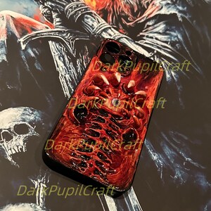 May include: A red and black phone case with a detailed image of a skull and bones. The case has the text "DarkPupilCraft" printed on it.