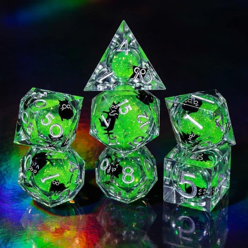 May include: A set of seven clear, multi-sided dice with a vibrant green interior and black cat silhouettes. The dice feature white numbers and are designed for tabletop gaming. The dice are arranged on a reflective surface.