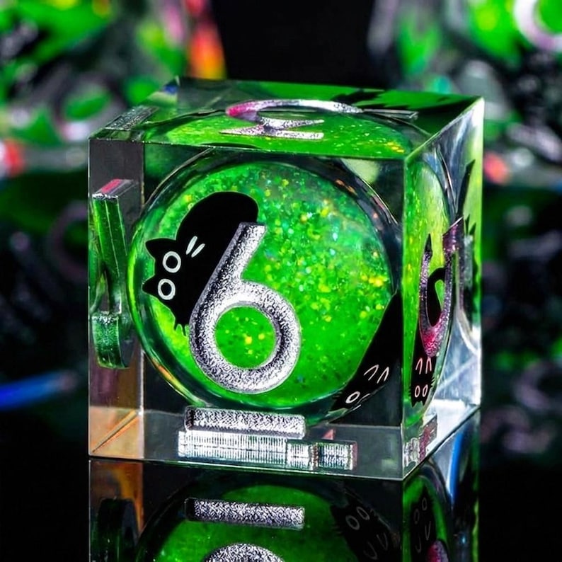 May include: A clear, square die with a green, glitter-filled interior. The number 6 is displayed in silver, with a black cat silhouette. The die is reflected on a mirrored surface, creating a unique visual effect.