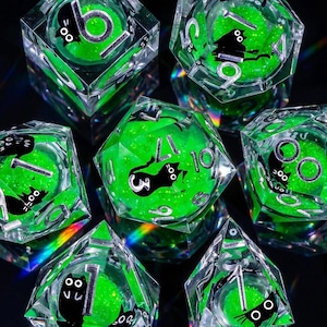 May include: Set of seven clear, multi-sided dice with a green glitter core and black cat illustrations. The dice feature white numbers and are designed for tabletop gaming. The dice are displayed on a dark surface.