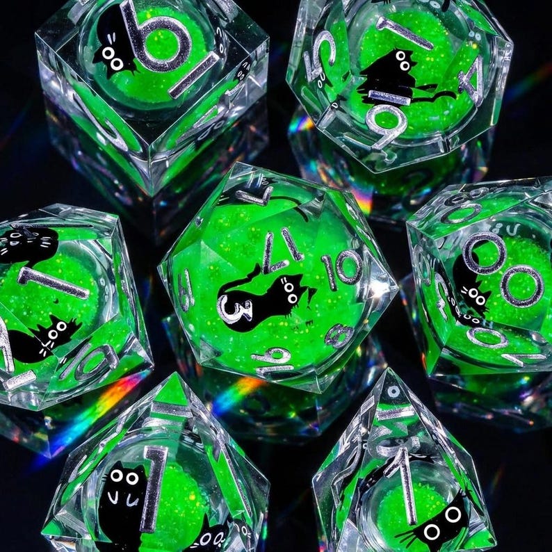May include: Set of seven clear, multi-sided dice with a green glitter core and black cat illustrations. The dice feature white numbers and are designed for tabletop gaming. The dice are displayed on a dark surface.