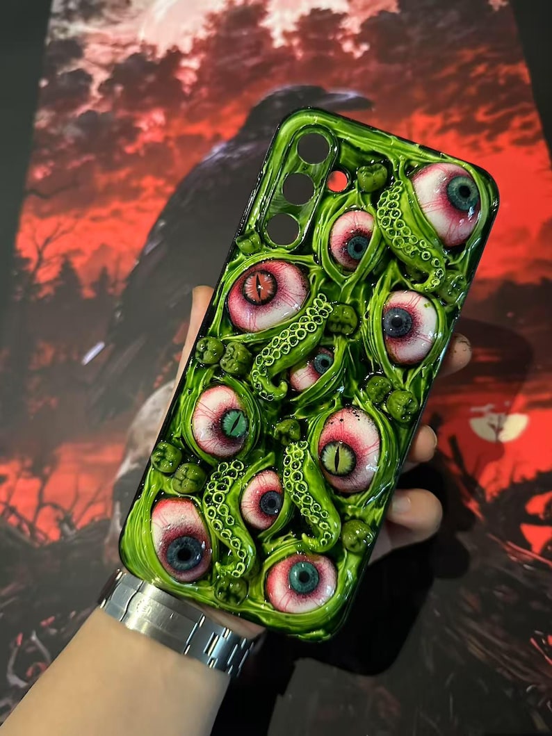 Op de afbeelding: Groene telefoonhoes met een gedetailleerd ontwerp van meerdere oogballen met rode, blauwe en groene irissen en groene tentakels. De hoes heeft een glanzende afwerking en een unieke, artistieke uitstraling.
