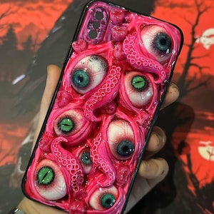 Op de afbeelding: Een roze telefoonhoesje met meerdere realistische oogballen met blauwe en groene irissen en roze tentakels. De hoes heeft een zwarte rand.