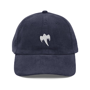 May include: Navy blue corduroy baseball cap featuring a white embroidered ghost design on the front. The cap has a curved brim and an adjustable strap at the back. A stylish and comfortable accessory for casual wear.