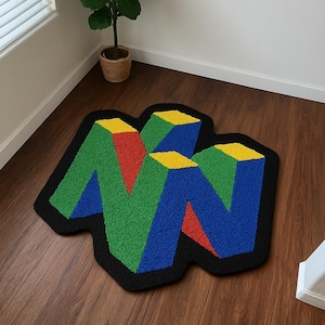 May include: A colorful rug featuring the iconic Nintendo 64 logo. The rug has a black border and the logo is rendered in green, blue, red, and yellow. The rug is placed on a wooden floor.