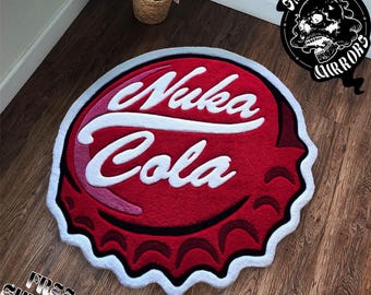 May include: A red, white, and pink Nuka Cola bottle cap shaped rug. The rug features the words "Nuka Cola" in white, stylized lettering. The rug has a white border and is on a wooden floor.