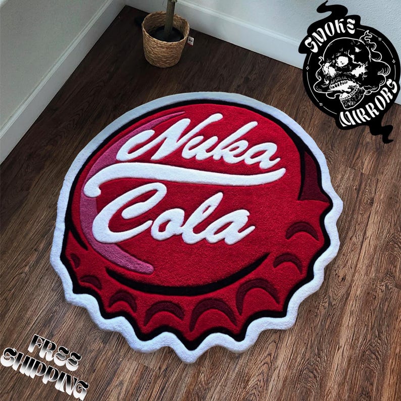 May include: A red, white, and pink Nuka Cola bottle cap shaped rug. The rug features the words "Nuka Cola" in white, stylized lettering. The rug has a white border and is on a wooden floor.