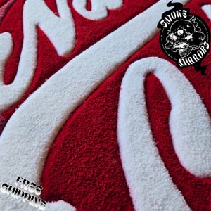 May include: Close-up of a red and white rug with the words "Smoke & Mirrors" in a stylized font. The rug has a plush texture and a skull logo. The words "Free Shipping" are also visible.