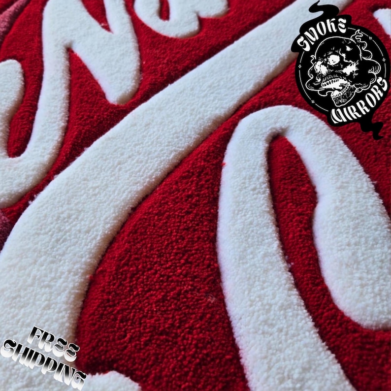 May include: Close-up of a red and white rug with the words "Smoke & Mirrors" in a stylized font. The rug has a plush texture and a skull logo. The words "Free Shipping" are also visible.
