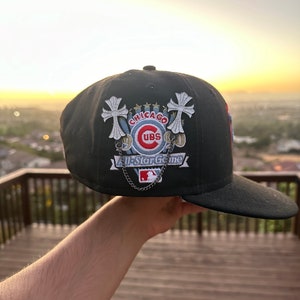 May include: Black baseball cap featuring the Chicago Cubs logo and "All-Star Game" text. The cap has a curved brim and decorative silver chain. The design includes embroidered crosses and stars.