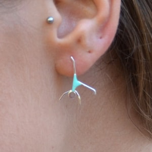 以下が含まれることがあります： ターコイズブルーのアクセントが付いたシルバーのイヤリングのペア。イヤリングは逆立ちをしている人の形をしています。