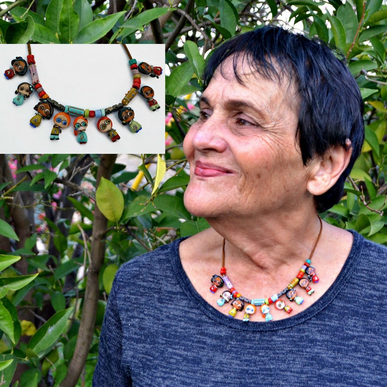 May include: A colorful necklace with small, painted figures of people hanging from it. The necklace is made of brown leather cord and colorful beads.