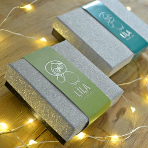 May include: Two silver glitter gift boxes with green and blue lids. The lids have a cartoon animal design and the text "LILA - Save the Owl" printed on them.