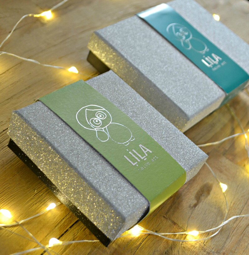 May include: Two silver glitter gift boxes with green and blue lids. The lids have a cartoon animal design and the text "LILA - Save the Owl" printed on them.