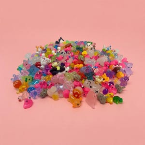 May include: A large collection of miniature animal figurines in various colors and translucent finishes. The assortment includes tiny ducks, bears, frogs, and other creatures made of smooth plastic, piled together in a dense, colorful heap.