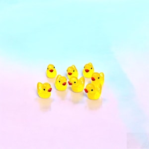 May include: A collection of eight miniature yellow rubber ducks, each featuring a bright orange beak and small black eyes. These tiny figurines are arranged in a loose cluster, showcasing their smooth, rounded bodies and classic duck shape.