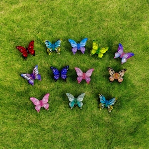 May include: A collection of colorful butterfly figurines in various shades of red, blue, purple, pink, and yellow. The butterflies are arranged on a bed of green grass, showcasing their intricate wing patterns and details.