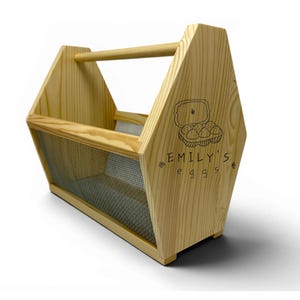 A clean studio photograph shows the handcrafted pine basket with its custom laser engraved front panel, breathable wire mesh sides and rounded dowel handle. This personalized egg collection basket is a handmade farmhouse egg gathering basket, a solid pine wood egg and produce basket with breathable metal mesh sides, a smooth sanded dowel carry handle, and a laser engraved front panel, about 12 inches long, 7.5 inches wide and 10 inches tall. A custom chicken egg basket, engraved egg holder...