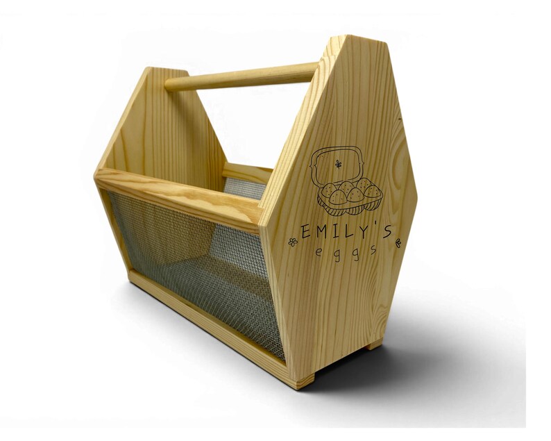 A clean studio photograph shows the handcrafted pine basket with its custom laser engraved front panel, breathable wire mesh sides and rounded dowel handle. This personalized egg collection basket is a handmade farmhouse egg gathering basket, a solid pine wood egg and produce basket with breathable metal mesh sides, a smooth sanded dowel carry handle, and a laser engraved front panel, about 12 inches long, 7.5 inches wide and 10 inches tall. A custom chicken egg basket, engraved egg holder...