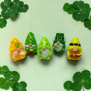 May include: A collection of five St. Patrick's Day gnome figurines in shades of green and yellow. Each gnome has a white beard and a hat, with some holding lucky charms. The background is a light green with shamrock accents.