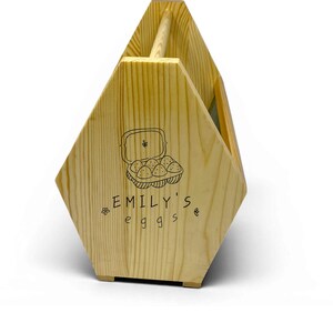 A clean studio photograph shows the handcrafted pine basket with its custom laser engraved front panel, breathable wire mesh sides and rounded dowel handle. This personalized egg collection basket is a handmade farmhouse egg gathering basket, a solid pine wood egg and produce basket with breathable metal mesh sides, a smooth sanded dowel carry handle, and a laser engraved front panel, about 12 inches long, 7.5 inches wide and 10 inches tall. A custom chicken egg basket, engraved egg holder...