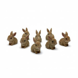 May include: A collection of eight small, tan-colored rabbit figurines. The rabbits are in various poses, some sitting and others standing, with their ears perked up. The figurines are detailed and appear to be made of a resin or similar material.