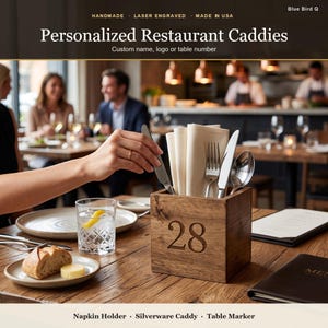 May include: A square wooden restaurant caddy featuring the laser-engraved number 28 on the front. The caddy holds beige cloth napkins, a silver fork, a silver knife, and a silver spoon. The text on the image reads Personalized Restaurant Caddies.