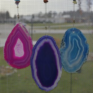 May include: Three agate slice wind chimes, each with a different color: pink, purple, and blue. The agate slices are suspended from a string with small beads.