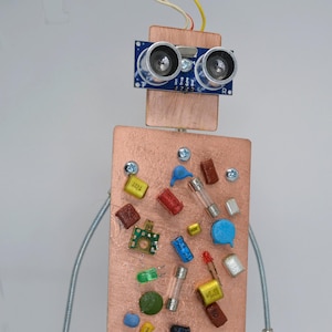 May include: A handmade robot sculpture constructed from copper plates, electronic components, and circuit boards. The robot features a rectangular body adorned with colorful capacitors and resistors, with wire arms and spring legs. The head has two sensor eyes.
