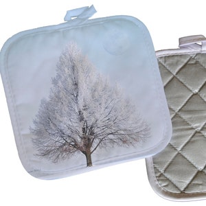 May include: Two pot holders, one with a quilted design and the other with a wintery tree design. The tree pot holder is light blue with a white tree and a white background.