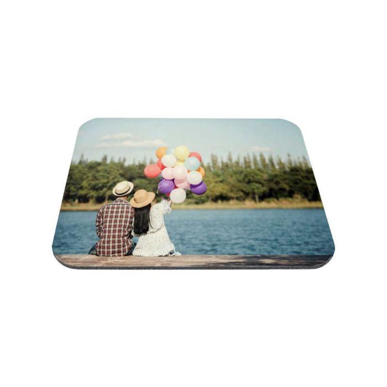 May include: A couple sits on a wooden dock by a lake, holding a bunch of colorful balloons. The man is wearing a plaid shirt and a straw hat, while the woman is wearing a white dress and a straw hat.
