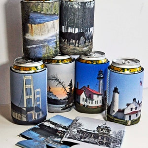 May include: A set of seven colorful can coolers with various images printed on them. The images include a waterfall, a forest, a bridge, a lighthouse, a sunset, and a building. The can coolers are made of foam and are designed to keep drinks cold.