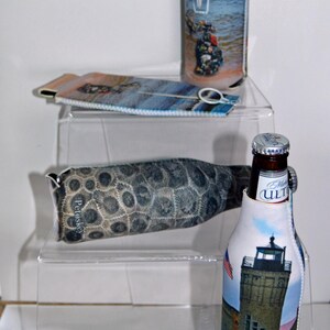 May include: Three different bottle coolers with zipper closures. The first cooler is blue and white with a picture of a boat. The second cooler is brown and white with a pattern of fossilized stones. The third cooler is white with a picture of a lighthouse. All three coolers have a zipper closure.