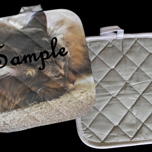 May include: A pair of gray and white quilted pot holders. One pot holder has a photo of a sleeping cat with the word "Sample" printed on it.