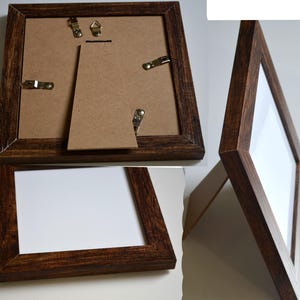 May include: A dark brown wooden picture frame with a white mat and a clear glass front. The frame has a easel back for tabletop display and hanging hardware on the back.