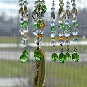 May include: A decorative wind chime with strands of clear, green, and amber-colored beads. The wind chime features a large, curved, translucent agate stone. The beads are strung on metal wires.