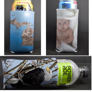 May include: Three different can coolers with various designs. The first cooler is blue with a brown outline of the state of Michigan. The second cooler is white with a baby wrapped in a white towel. The third cooler is a close-up of a bald eagle perched on a branch with a blue sky in the background. The cooler is wrapped around a clear plastic bottle with a green label that says "POWERADE POWER WATER".