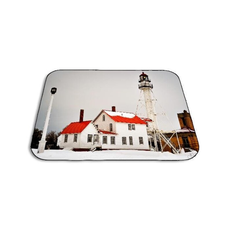 May include: A white lighthouse with a red roof stands tall against a cloudy sky. A smaller white building with a red roof is located to the left of the lighthouse. The buildings are covered in snow.