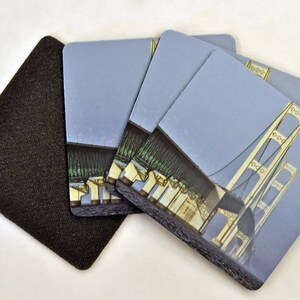 May include: Set of four coasters featuring a photograph of the Mackinac Bridge. The coasters are made of a cork-like material with a black backing.